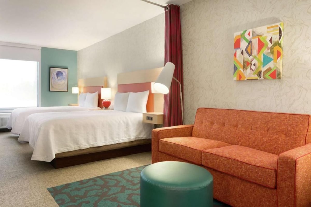 A hotel room with two beds, a sofa, a lamp, and a painting on the wall.