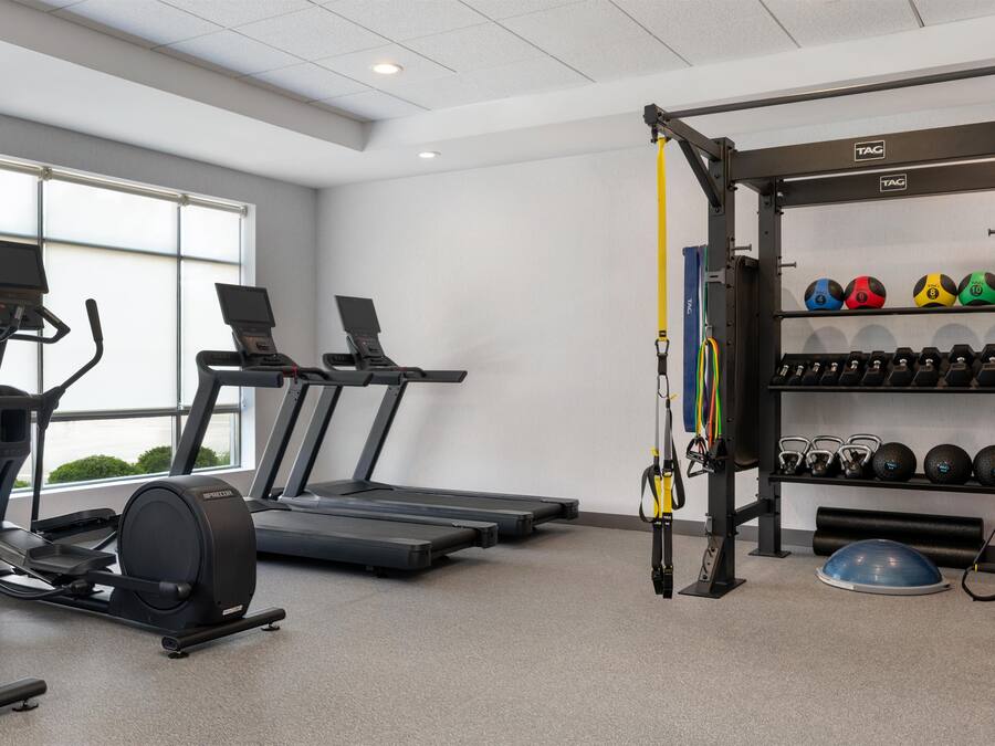Un gimnasio con cintas de correr, una máquina de remo, un entrenador TRX y discos de pesas.