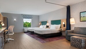 A hotel room with two beds, a desk with a chair, a sofa, and a patterned ottoman. - Home2 Suites Florence/Cincinnati Airport South, KY (Florence)