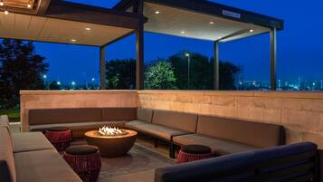 An outdoor seating area with a fire pit, cushioned benches, and a covered section with a clear sign.