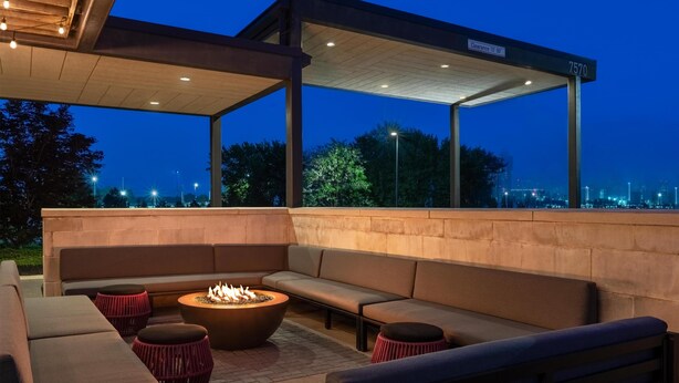 An outdoor seating area with a fire pit, cushioned benches, and a covered section with a clear sign. - Home2 Suites Florence/Cincinnati Airport South, KY (Florence)