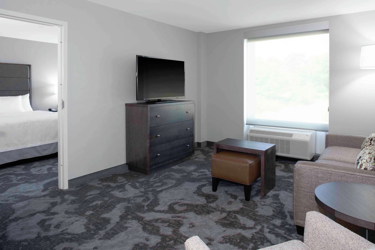 Ein Hotelzimmer mit Bett, Fernseher auf einer Kommode, einer Couch, einem kleinen Tisch und einem Fenster mit Blick.