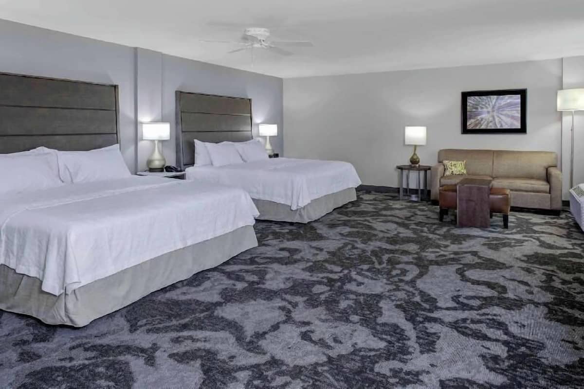 Ein Hotelzimmer mit zwei Betten, einer Couch, einem Deckenventilator und einem gemusterten Teppich.