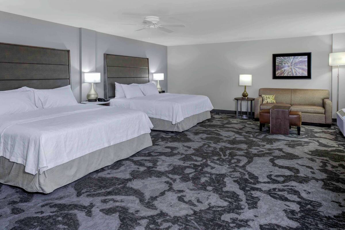 Ein Hotelzimmer mit zwei Betten, einer Couch, einem Deckenventilator und Teppichboden.