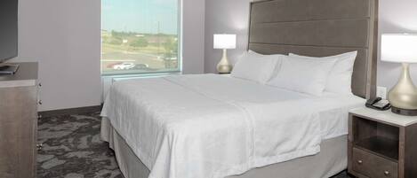 A hotel room with a large bed, two bedside lamps, a TV, and a view of the parking lot.