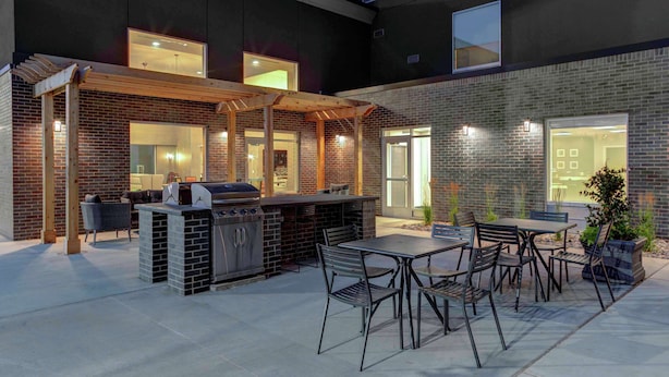 Un patio exterior con una parrilla, zona de estar y vistas al interior del edificio.