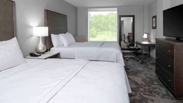 A hotel room with two beds, a desk, a television, and a large window.