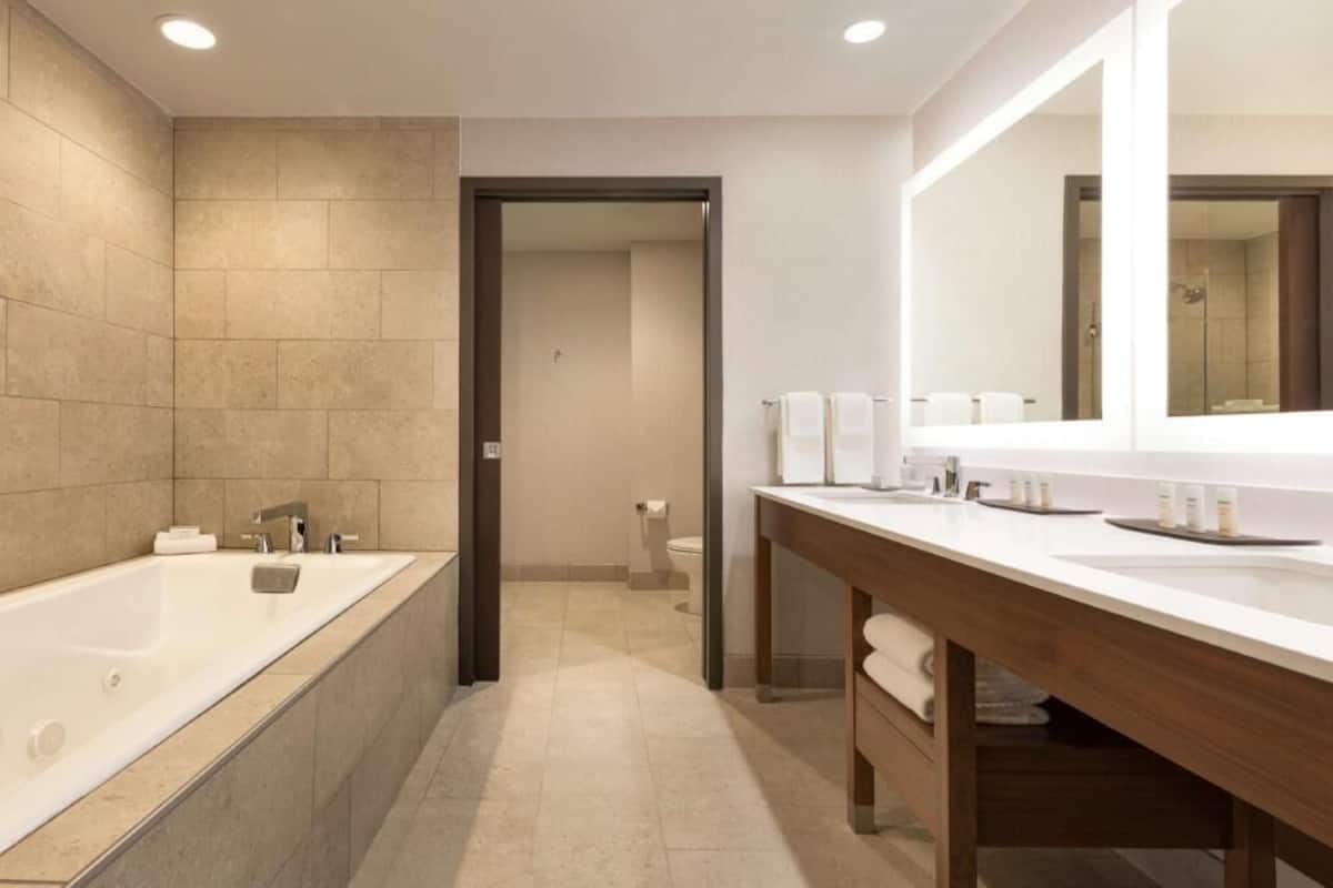 A modern bathroom with a large bathtub, a wooden vanity with a mirror, and a separate toilet area.