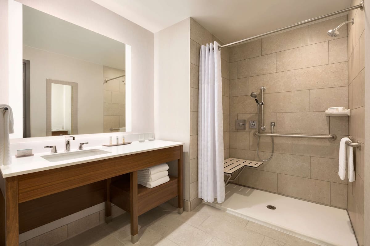 A modern bathroom with a large mirror, two sinks, a shower with a glass door, and a wooden vanity.