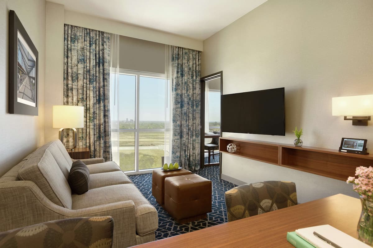 A hotel room with a sofa, ottoman, TV, and a dining table.