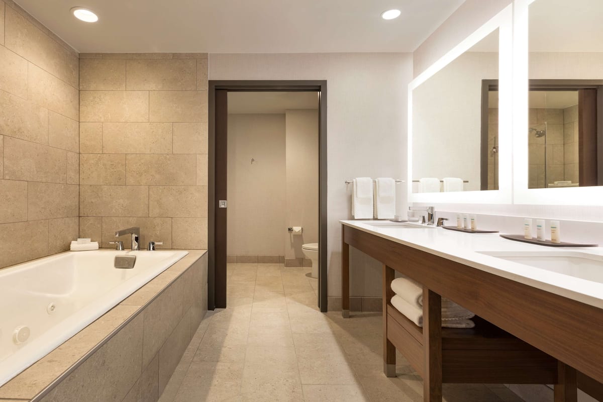 A modern bathroom with a large bathtub, a wooden vanity with a mirror, and a toilet.