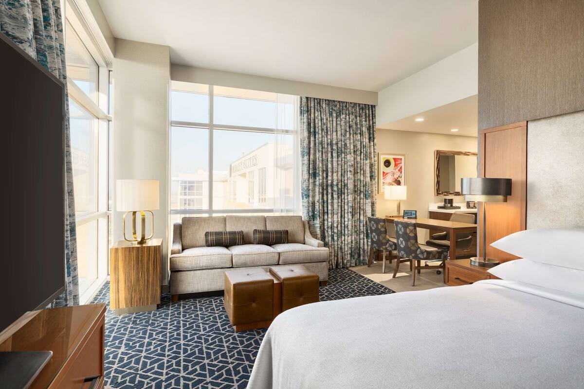 A hotel room with a bed, a sofa, a desk, a chair, and a TV.
