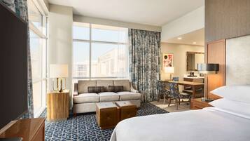 Quarto de hotel com cama, sofá, escrivaninha, cadeira e televisão.