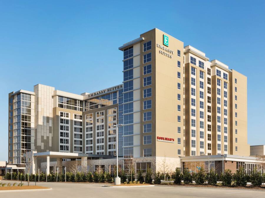 Un hotel de diverses plantes amb un cartell prominent d''Embassy Suites', una entrada coberta i un cel serè.