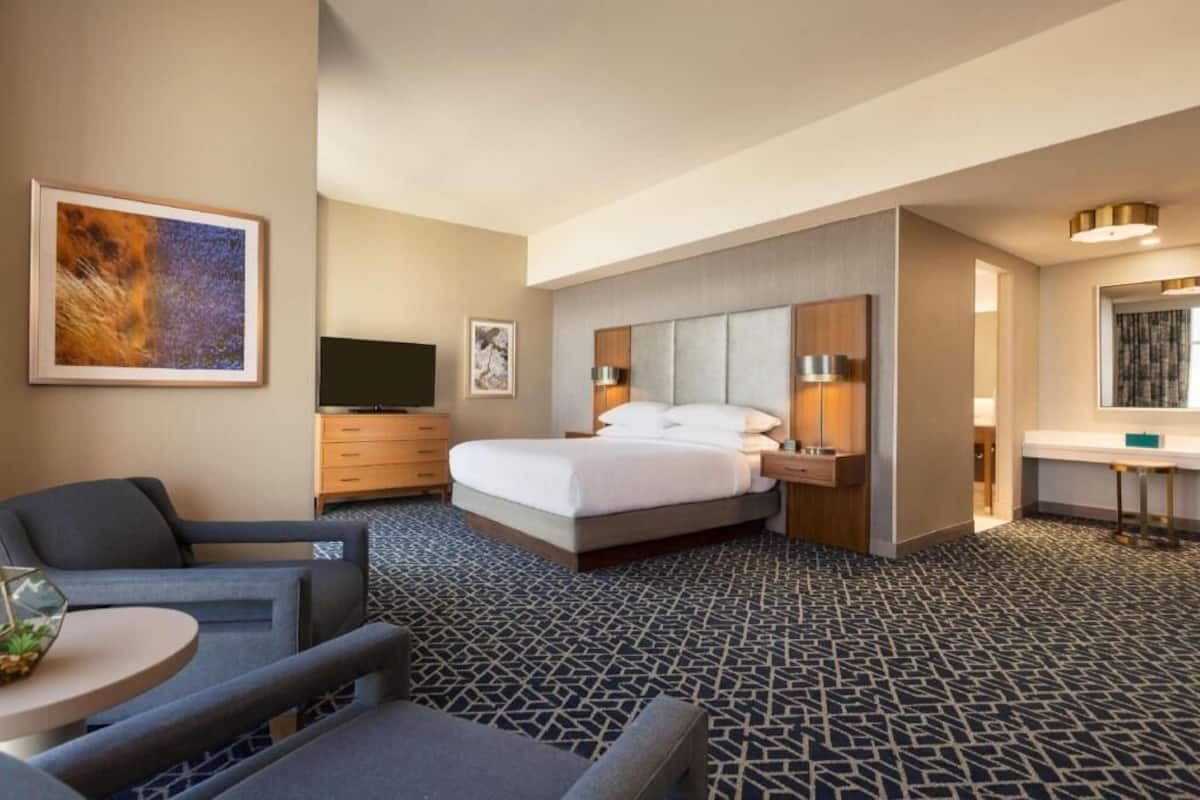 A hotel room with a bed, bedside tables, a TV, a desk, and a chair.