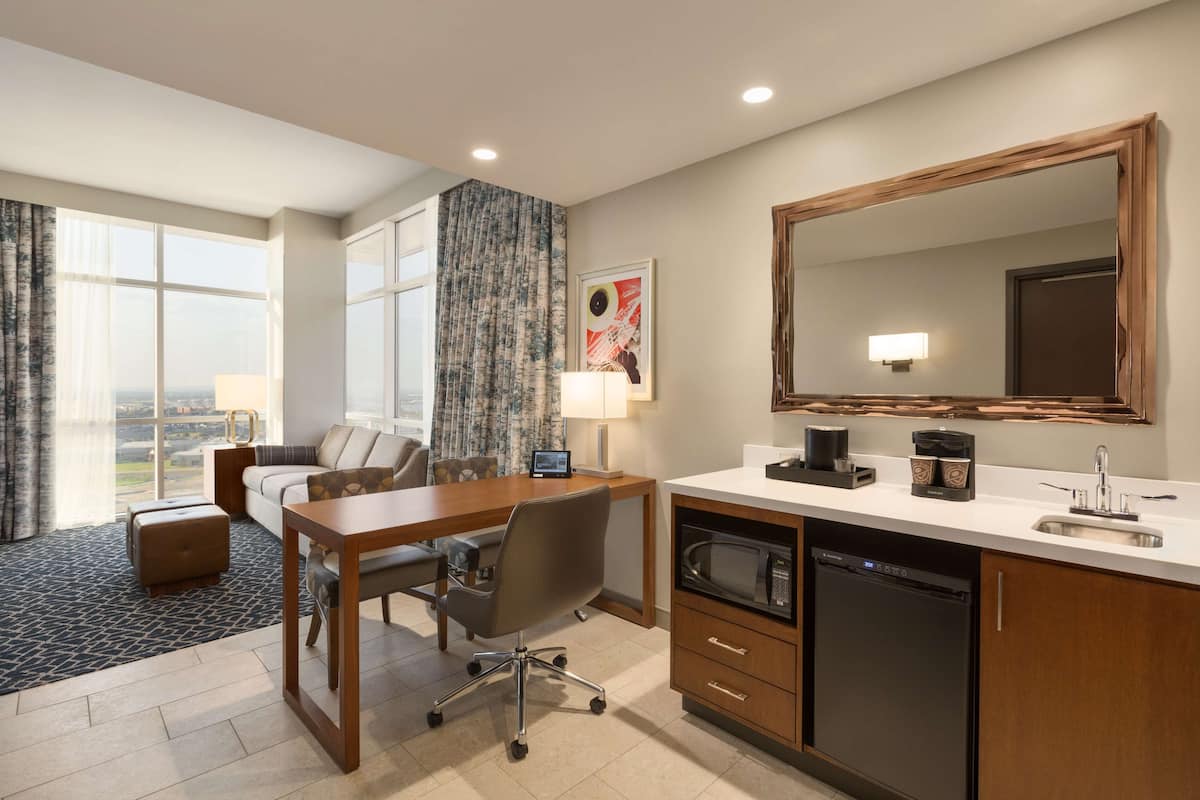 A hotel room with a desk, office chair, sofa, and a large window with a view.