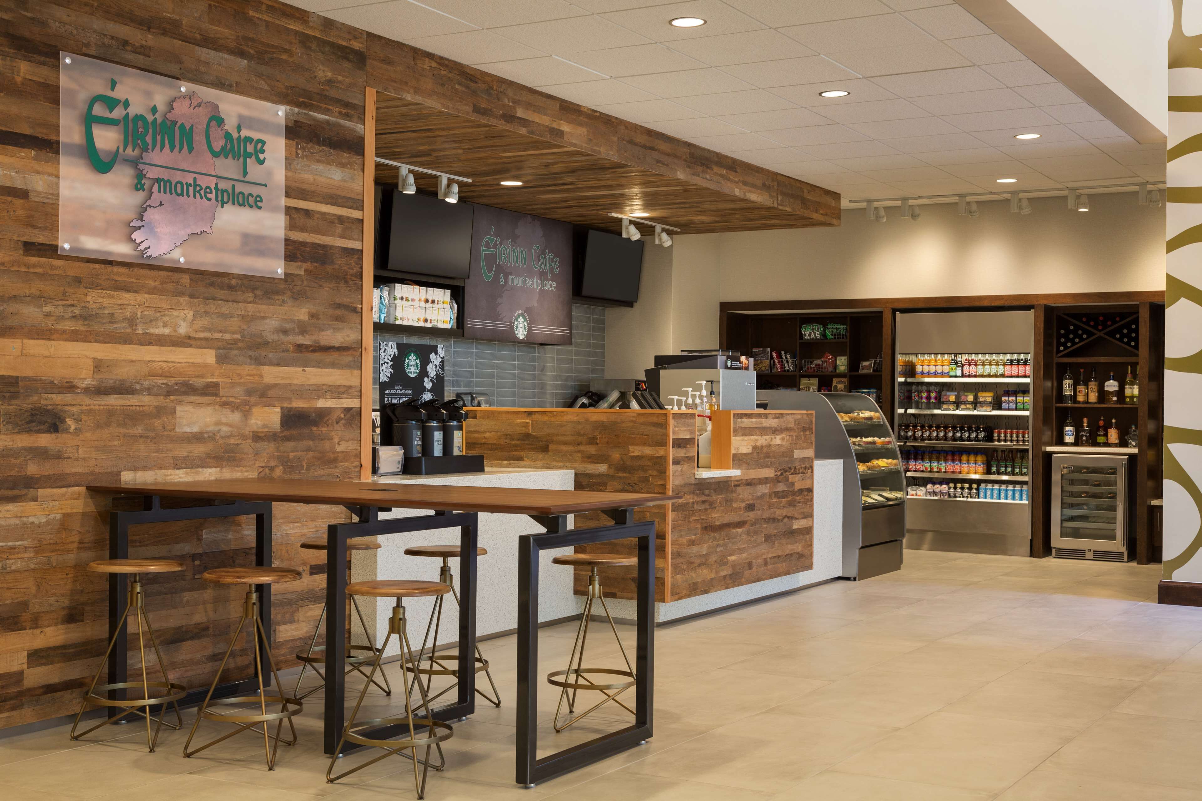 A modern coffee shop with a wooden interior, bar stools, a counter, and shelves stocked with beverages.
