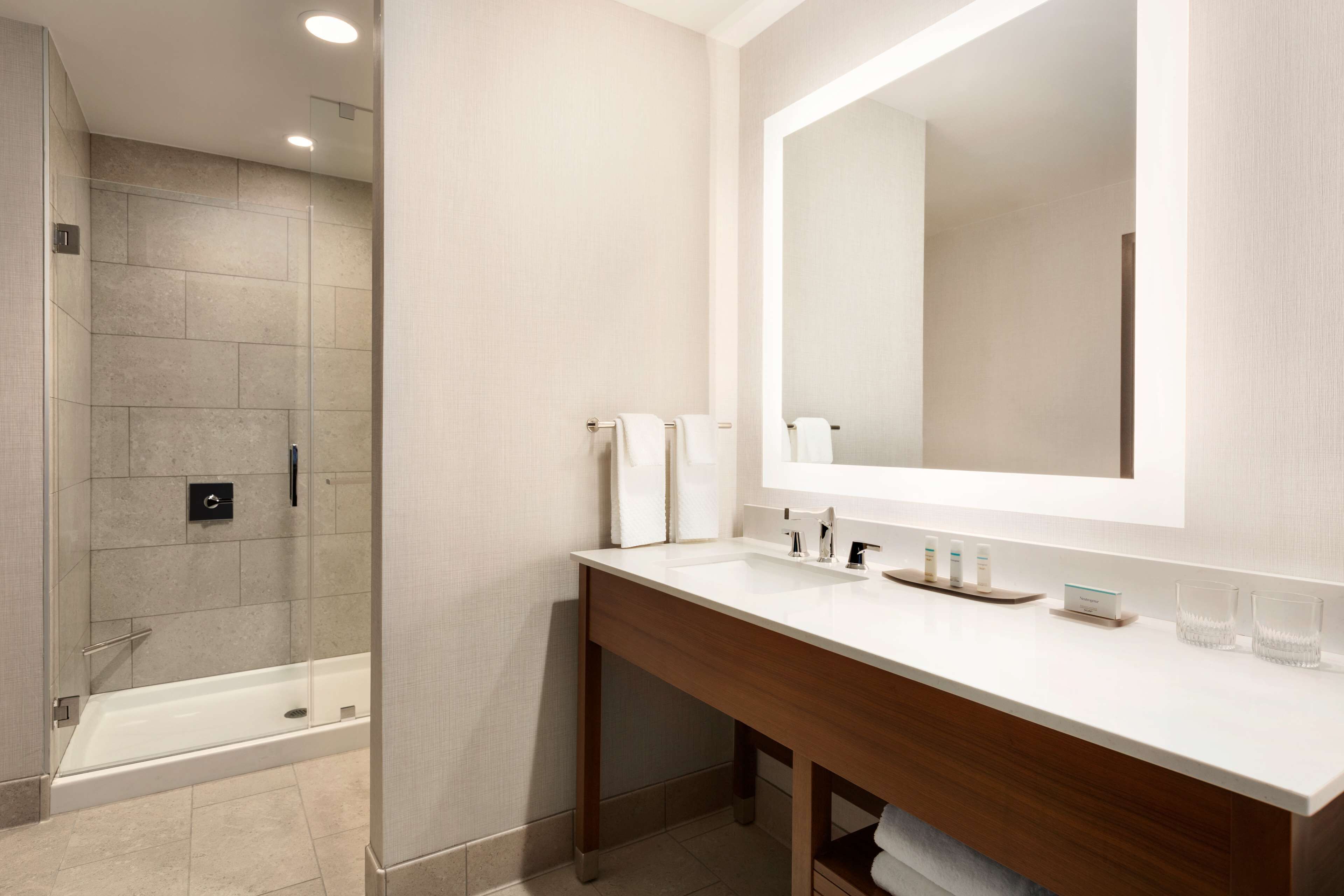 A modern bathroom with a glass-enclosed shower, a large mirror, and a wooden vanity.