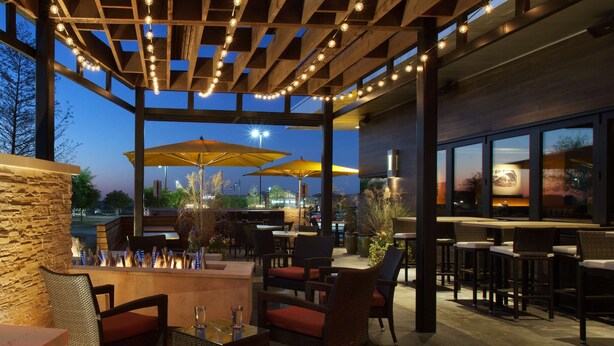 An outdoor patio area with wooden pergola, string lights, and outdoor seating. - Embassy Suites by Hilton Denton Convention Center (Denton)