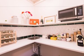 A kitchen with a white countertop, a stainless steel sink, a microwave, and various kitchen items. - Paravia Suite (Florence)