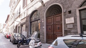 A street with parked cars and a scooter, a building with a sign reading "PALAZZO SODERINI," and a large wooden door. - Paravia Suite (Florence)