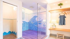 A room with a glass partition, a wooden floor, a tiled wall with a blue mosaic, a wooden shelf with clothes, and a small table with a lamp. - Paravia Suite (Florence)