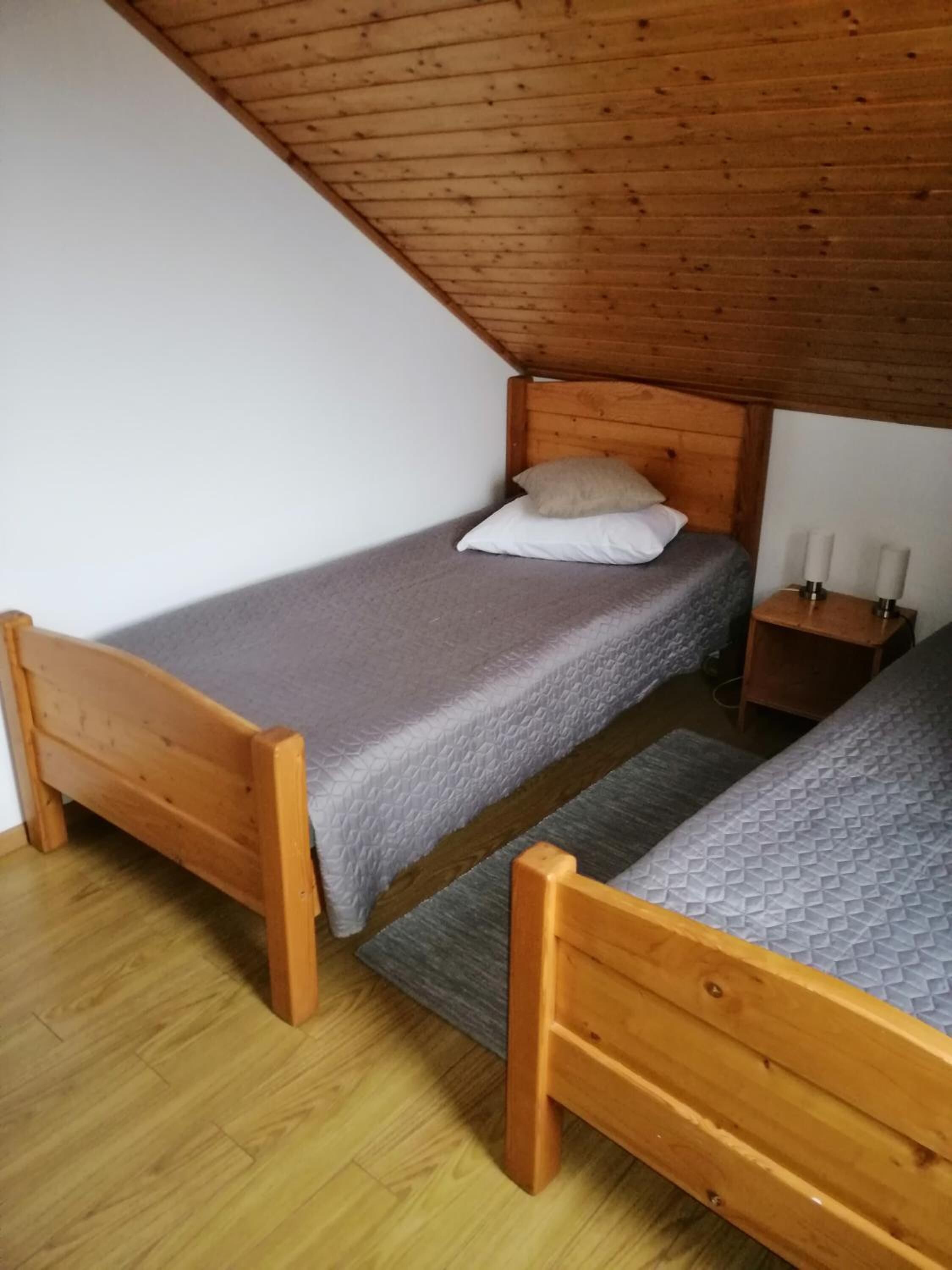 A small, wooden-floored room with two single beds, a nightstand with candles, and a sloped ceiling.
