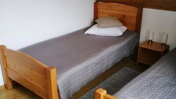 A small, wooden-floored room with two single beds, a nightstand with candles, and a sloped ceiling.