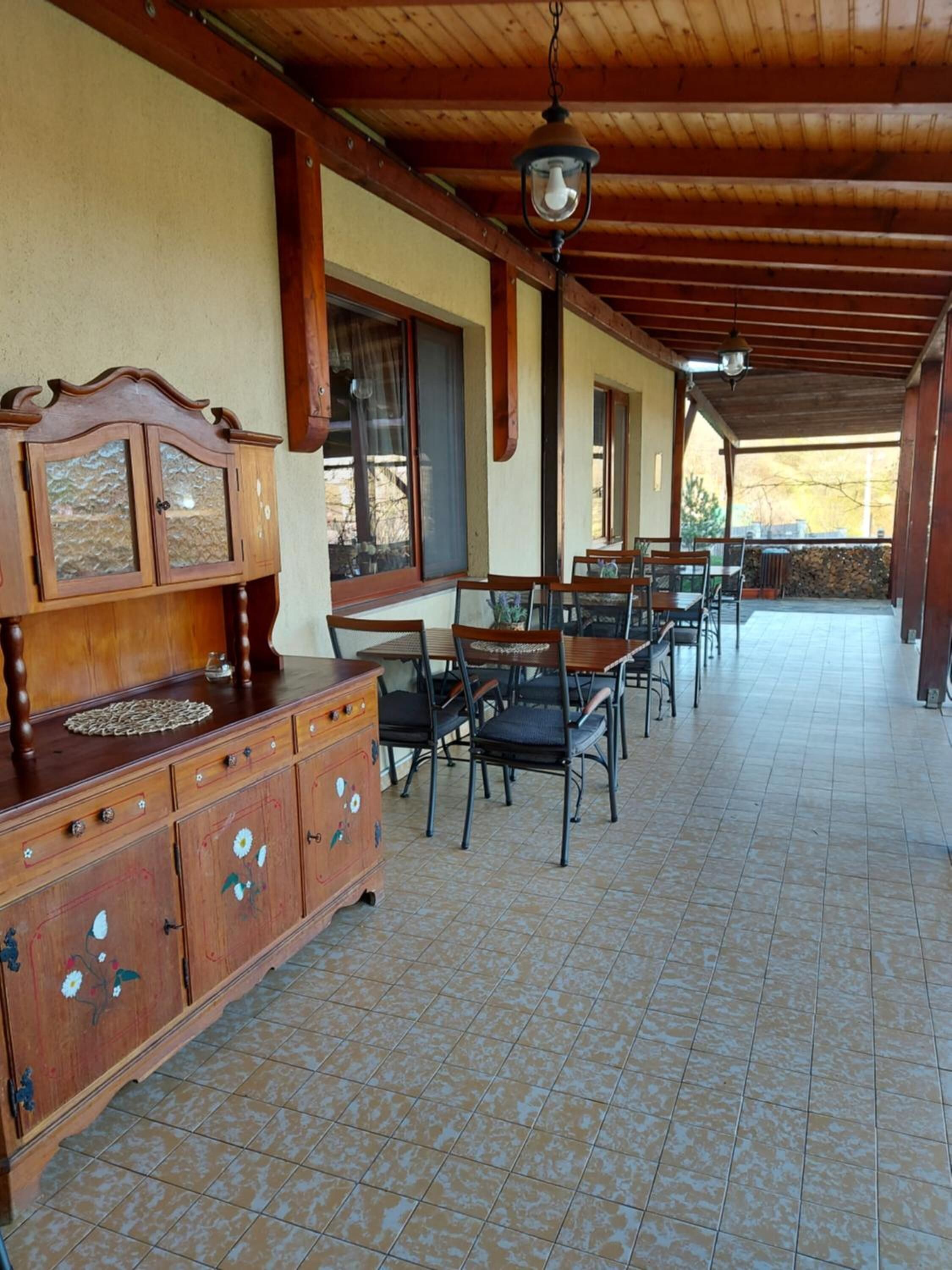 A covered patio area with a wooden table and chairs, a cabinet with floral designs, and a view of the outdoors.