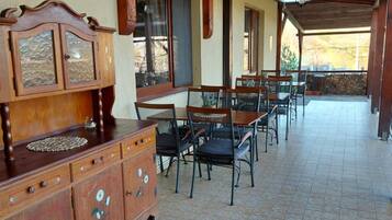 A covered patio area with a wooden table and chairs, a cabinet with floral designs, and a view of the outdoors.