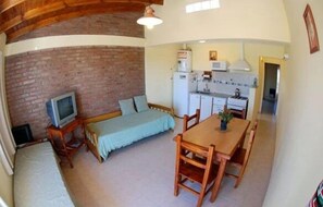 A compact living space with a brick wall, a television, a sofa, a dining table with chairs, and a kitchenette. - Complejo Turistico Andalhue (Puerto Madryn)