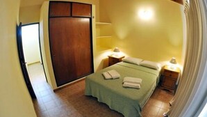Une chambre à coucher avec un lit, deux tables de chevet avec des lampes, une armoire et une porte.