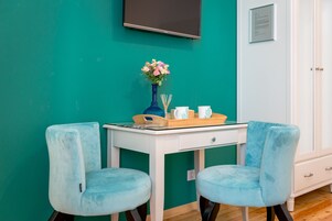 Ein türkisfarbenes Zimmer mit einem weißen Schreibtisch, zwei gleichgestimmten Stühlen, einer Blumenvase und einem gerahmten Dokument an der Wand.