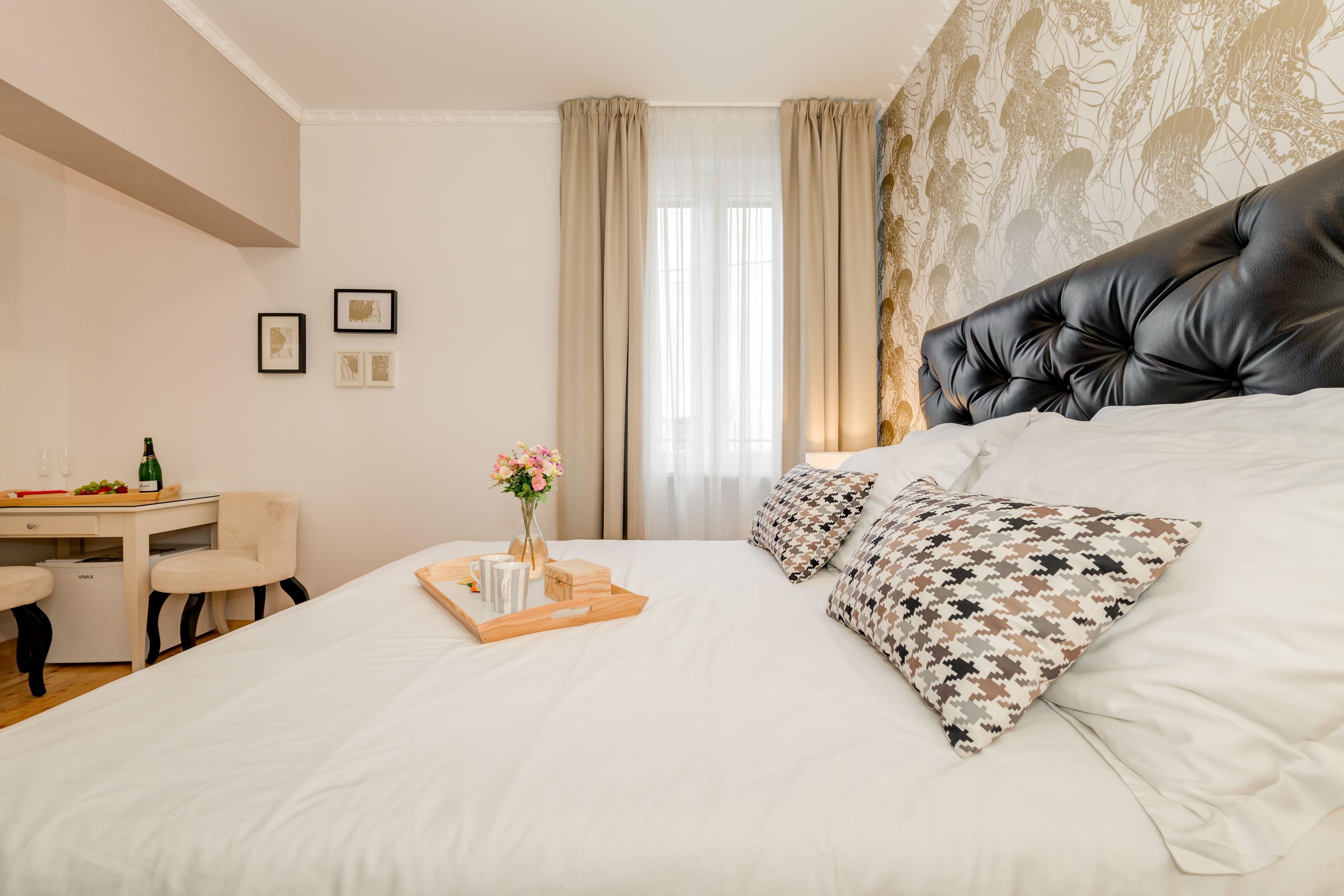 A neatly arranged hotel room with a large bed, a desk with a chair, and a window with curtains.