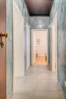 Ein Flur mit gemusterten Wänden und Fliesenboden, der zu einem Badezimmer mit Toilette und Waschbecken führt.