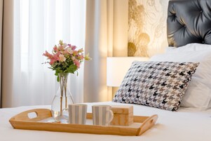 Ein ordentlich gedeckter Frühstückstisch mit Blumen, zwei gestreifte Tassen und einer Kiste auf einem Bett mit einem gemusterten Kopfkissen und einem Kopfteil.