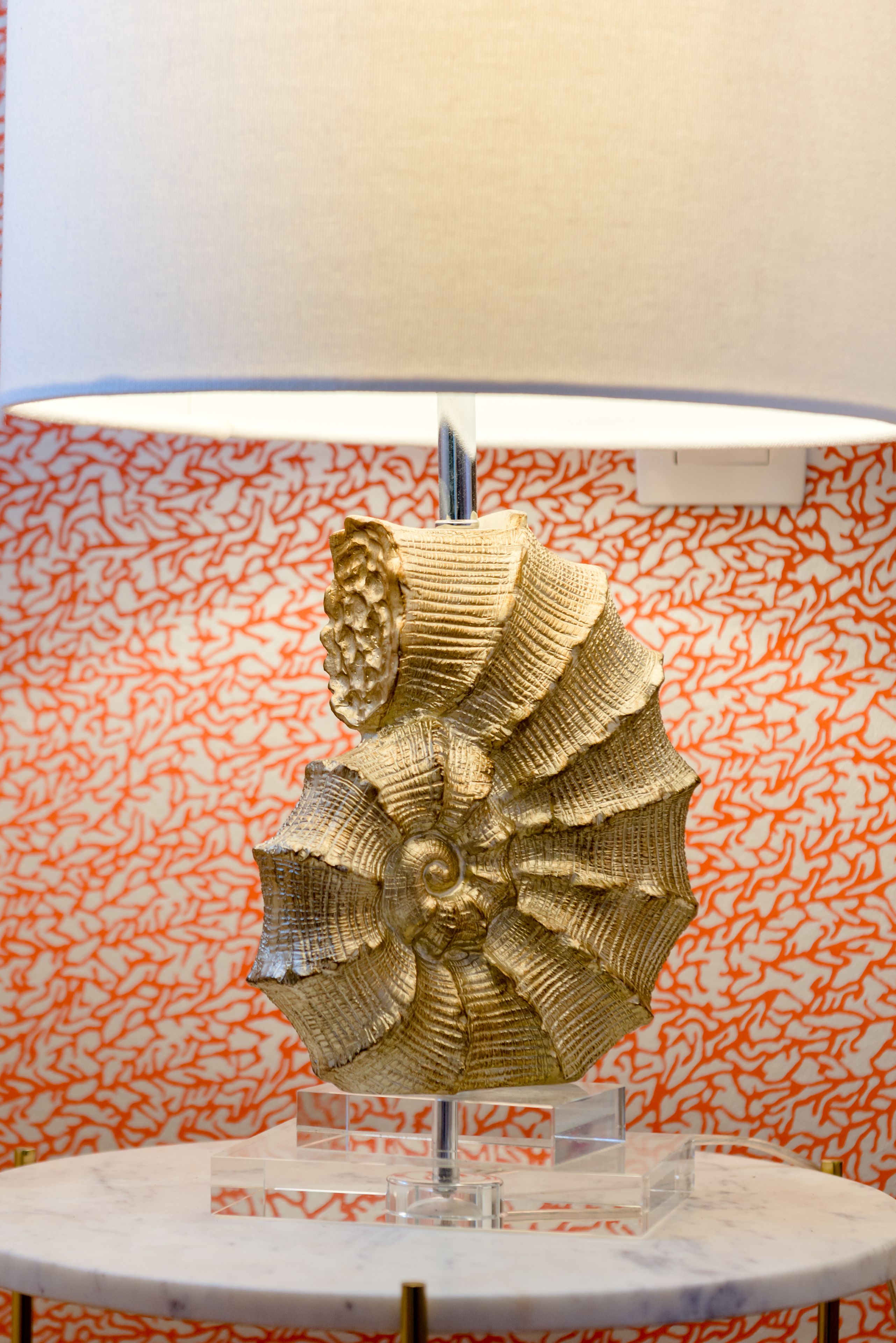 A sculpture on a marble pedestal in a room with patterned wallpaper.