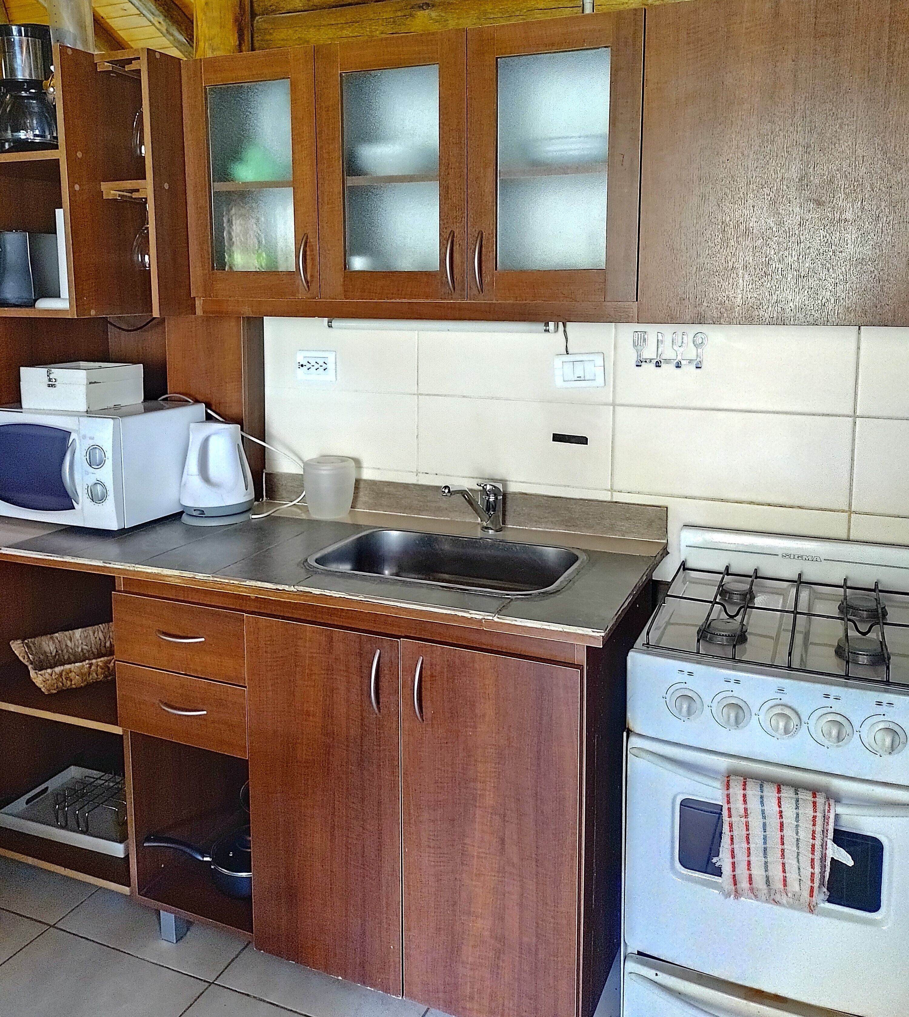 A kitchen with wooden cabinets, a white stove, a sink, and a microwave.
