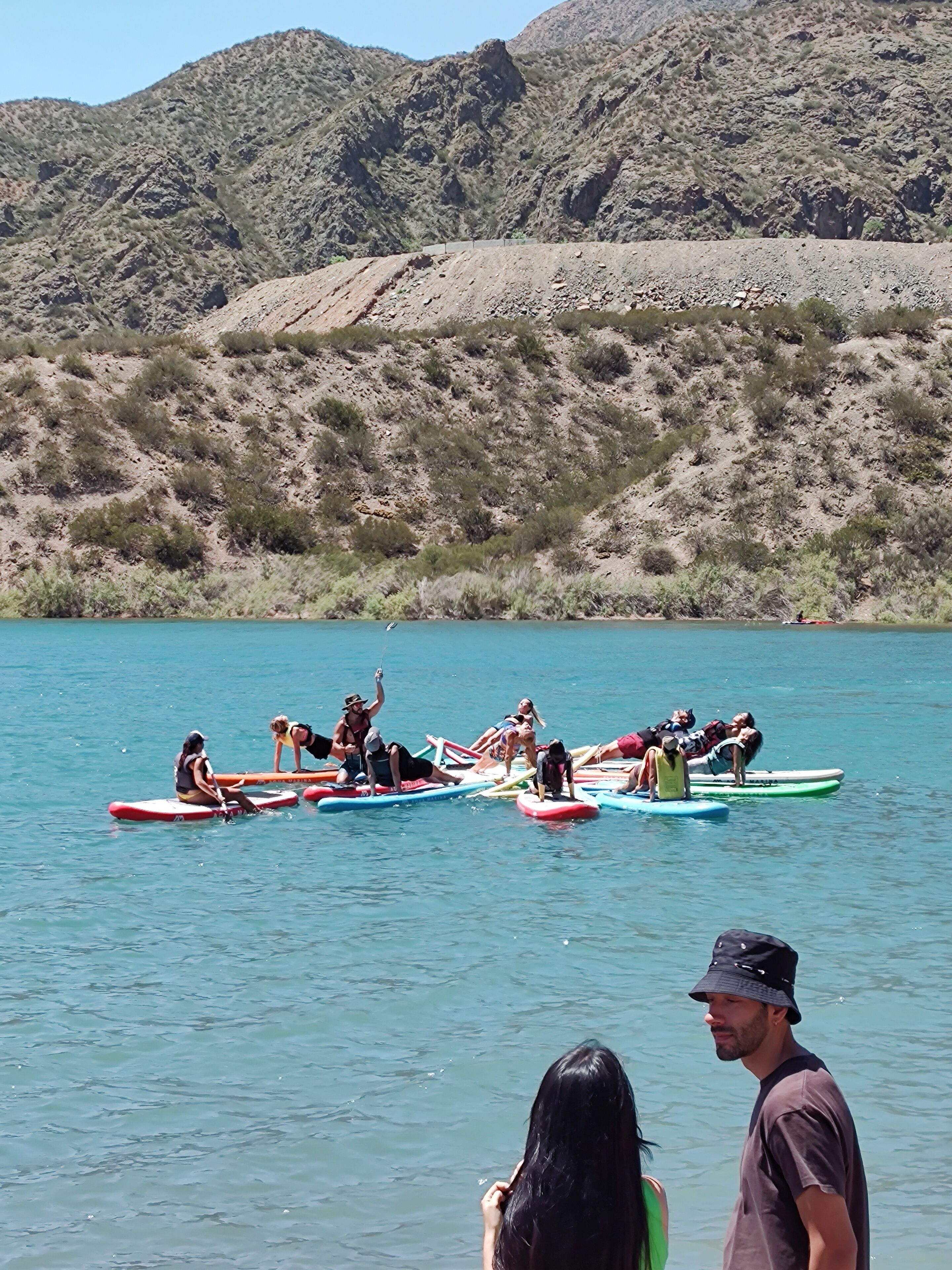 Un groupe de personnes sur des planches de surf, sur une étendue d’eau, avec une chaîne de montagnes en arrière-plan.