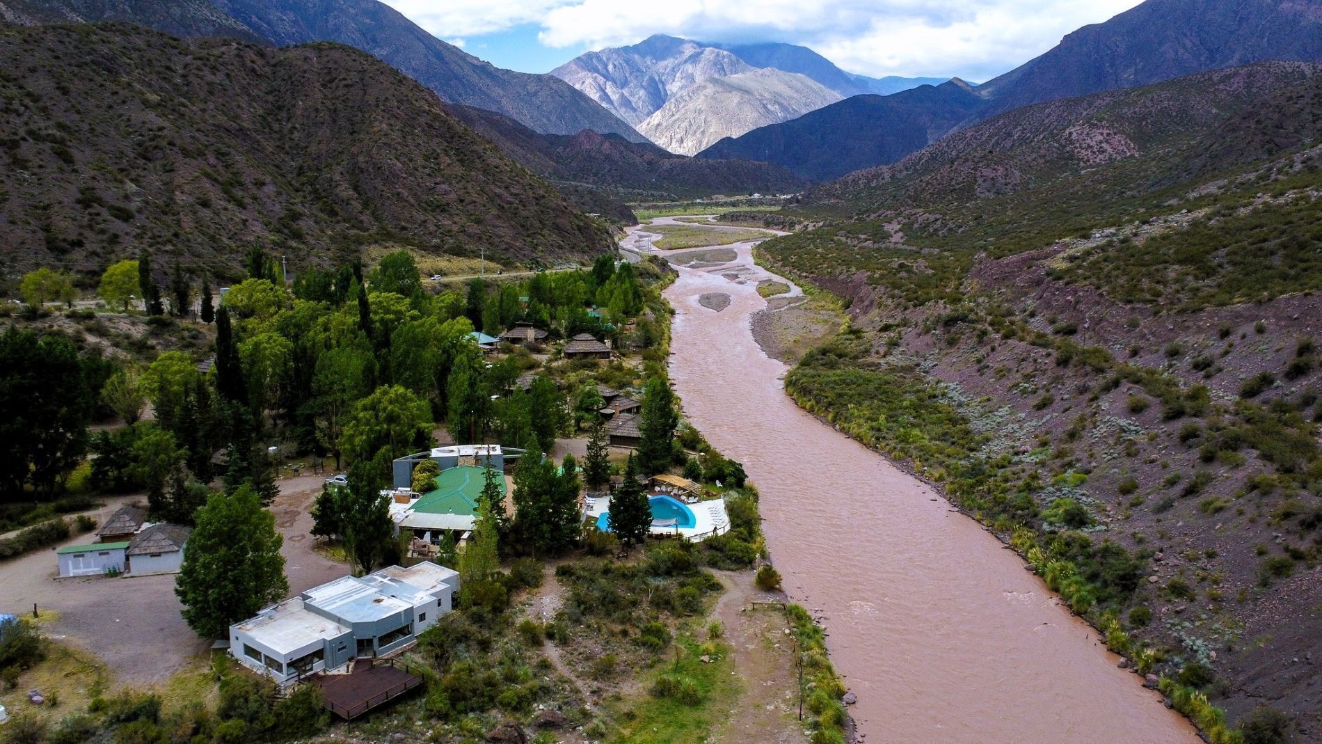 A riverside property with a swimming pool, surrounded by mountains and greenery.