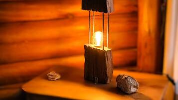 Interior rústico de una cabaña de madera, con una mesa central de madera que sostiene un farol, rodeada de libros y un pequeño adorno.