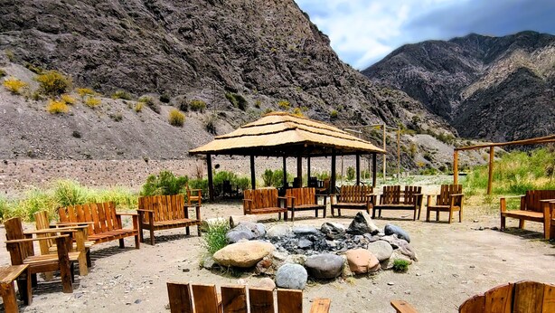 An outdoor seating area with wooden benches and a covered pavilion, set against a mountainous backdrop. - Mendoza Sol y Nieve (Potrerillos)