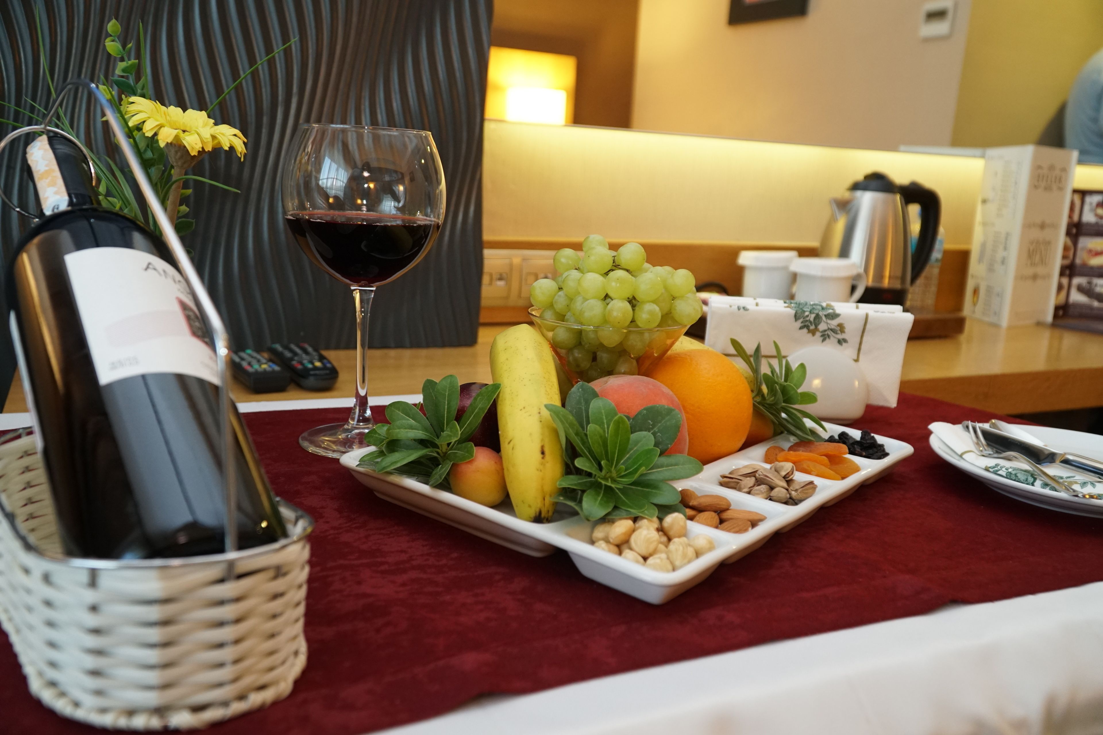 Uma mesa com uma garrafa de vinho, uma taça de vinho tinto, um prato de frutas e uma cafeteira.