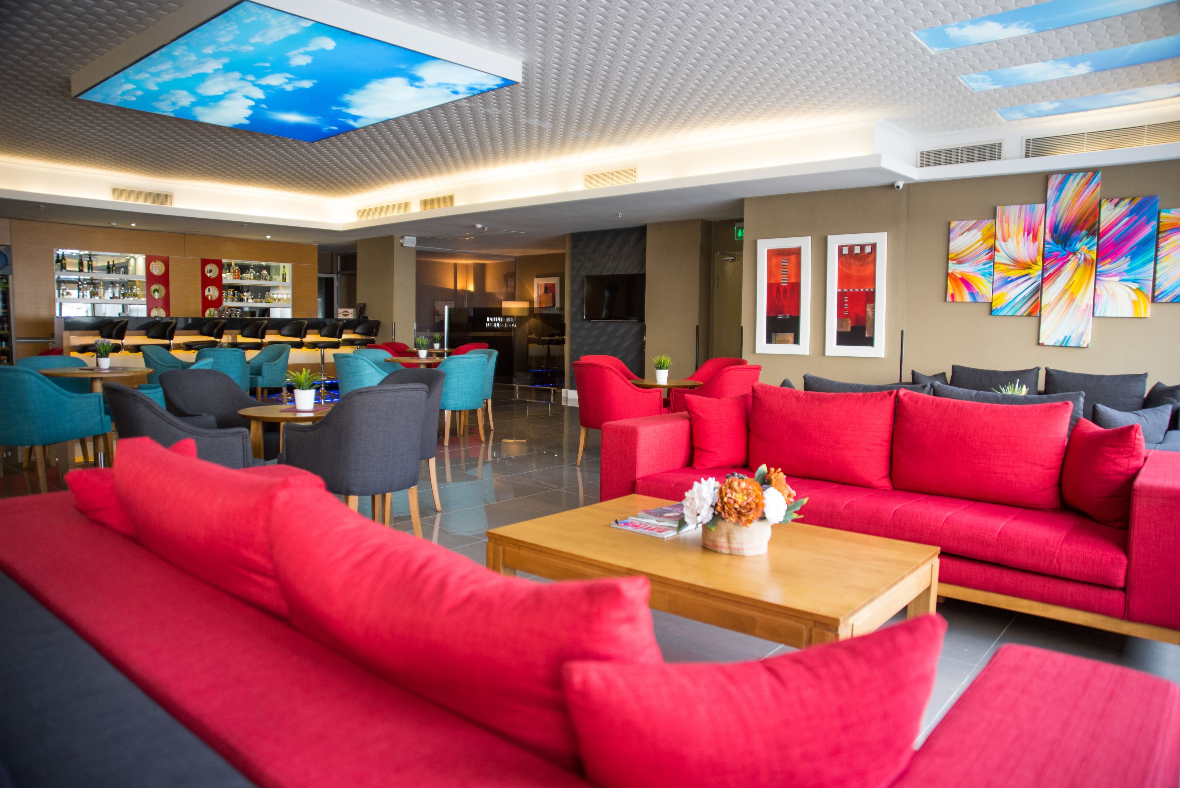 Eine moderne Hotelhalle mit roten Sofas, Türkis-farbenen Sesseln und einer Bar.