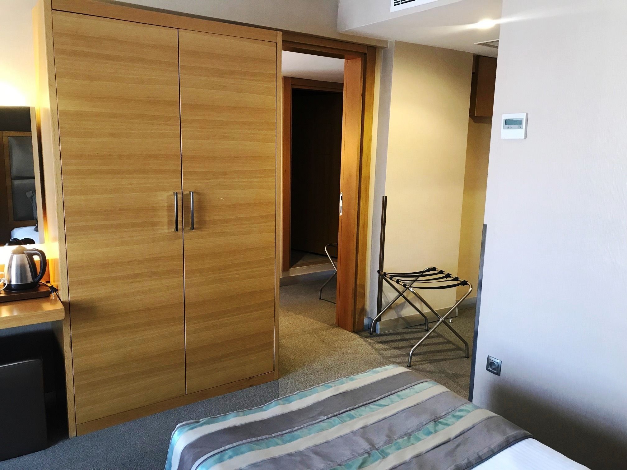 A hotel room with a wardrobe, a bed, a kettle, and a drying rack.