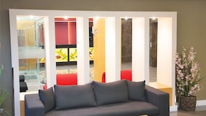 A reception area with a grey sofa, a potted plant, and a glass partition with colorful artwork. - Efeler Hotel (Aydin)