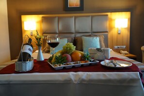 A neatly arranged breakfast tray with fruits, nuts, and a bottle of wine on a bed with a red blanket. - Efeler Hotel (Aydin)