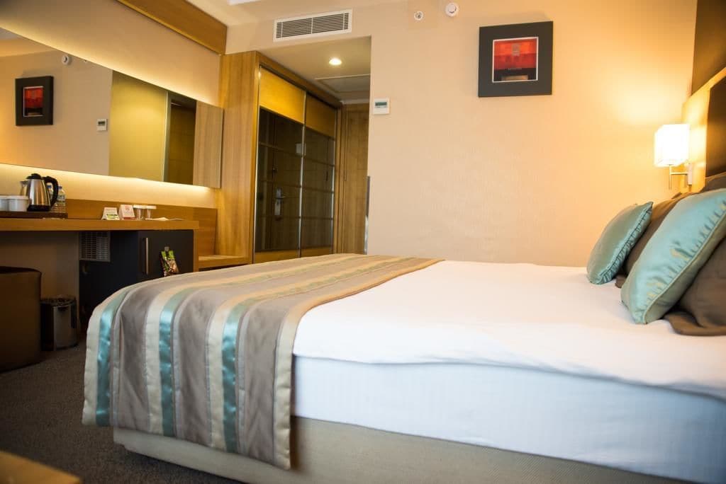 Habitación de hotel con cama, escritorio con cafetera, espejo y puerta al baño.