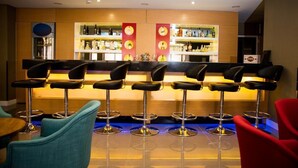 A bar area with multiple stools and a bar counter, shelves with bottles, and a refrigerator. - Efeler Hotel (Aydin)