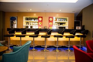 Uma área de bar com vários bancos e balcão, prateleiras com garrafas e uma geladeira.